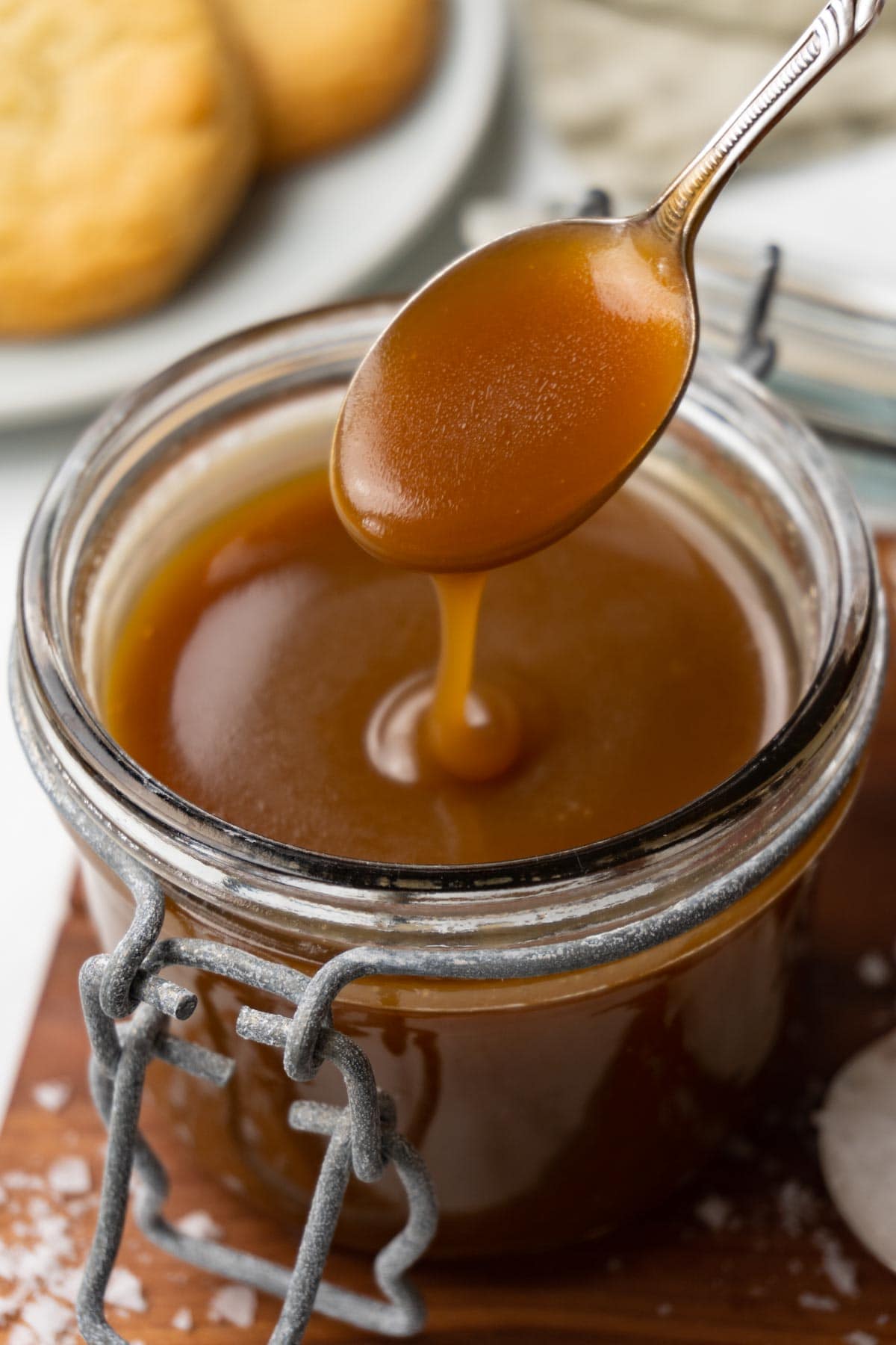 A glass jar filled with butterscotch sauce on a wooden board. A silver spoon is spooning out some sauce from the jar.