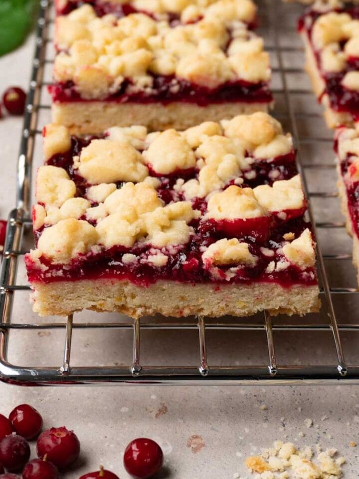 Cranberry crumble bars on a metal cooling rack, fresh cranberries are lying around.