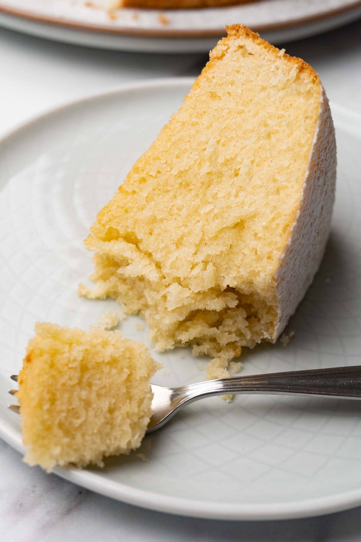 A piece of cake dusted with powdered sugar on a small round serving plate. Several bites were taken.