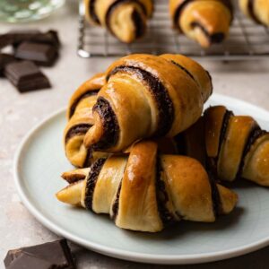 Crescents with chocolate filling on a plate. A few pieces of dark chocolate are lying around the plate.