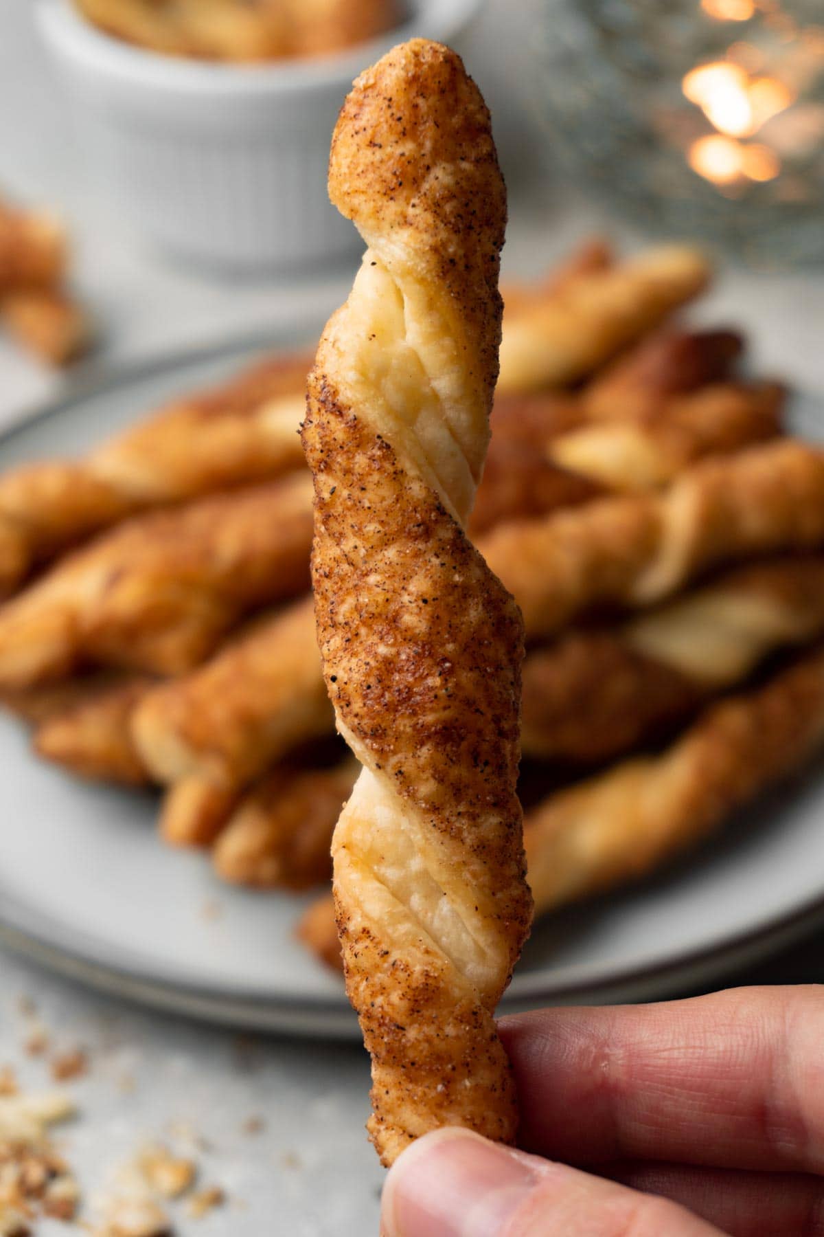 A hand is holding a pastry twist with cinnamon sugar topping. More twists are on the background.