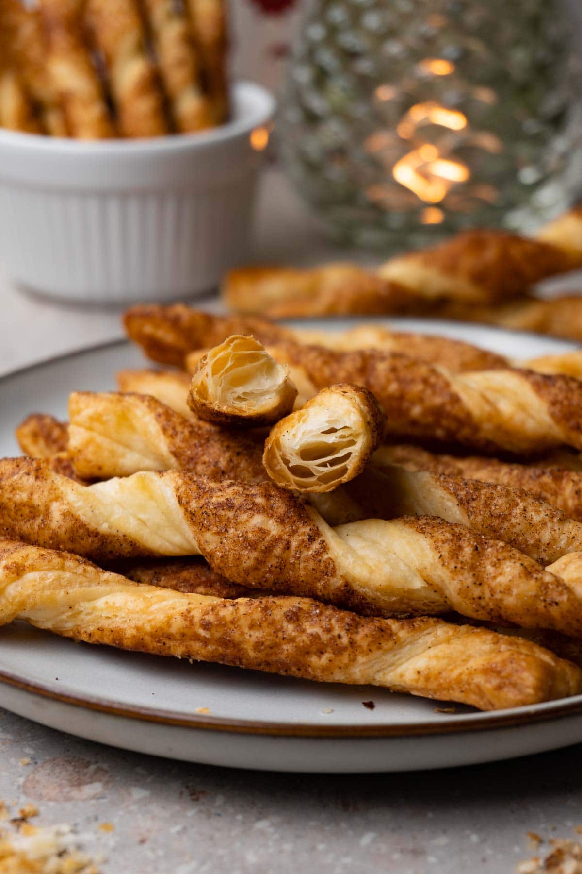 Puff pastry twists with cinnamon sugar topping on a round plate. One stick was broken in half.