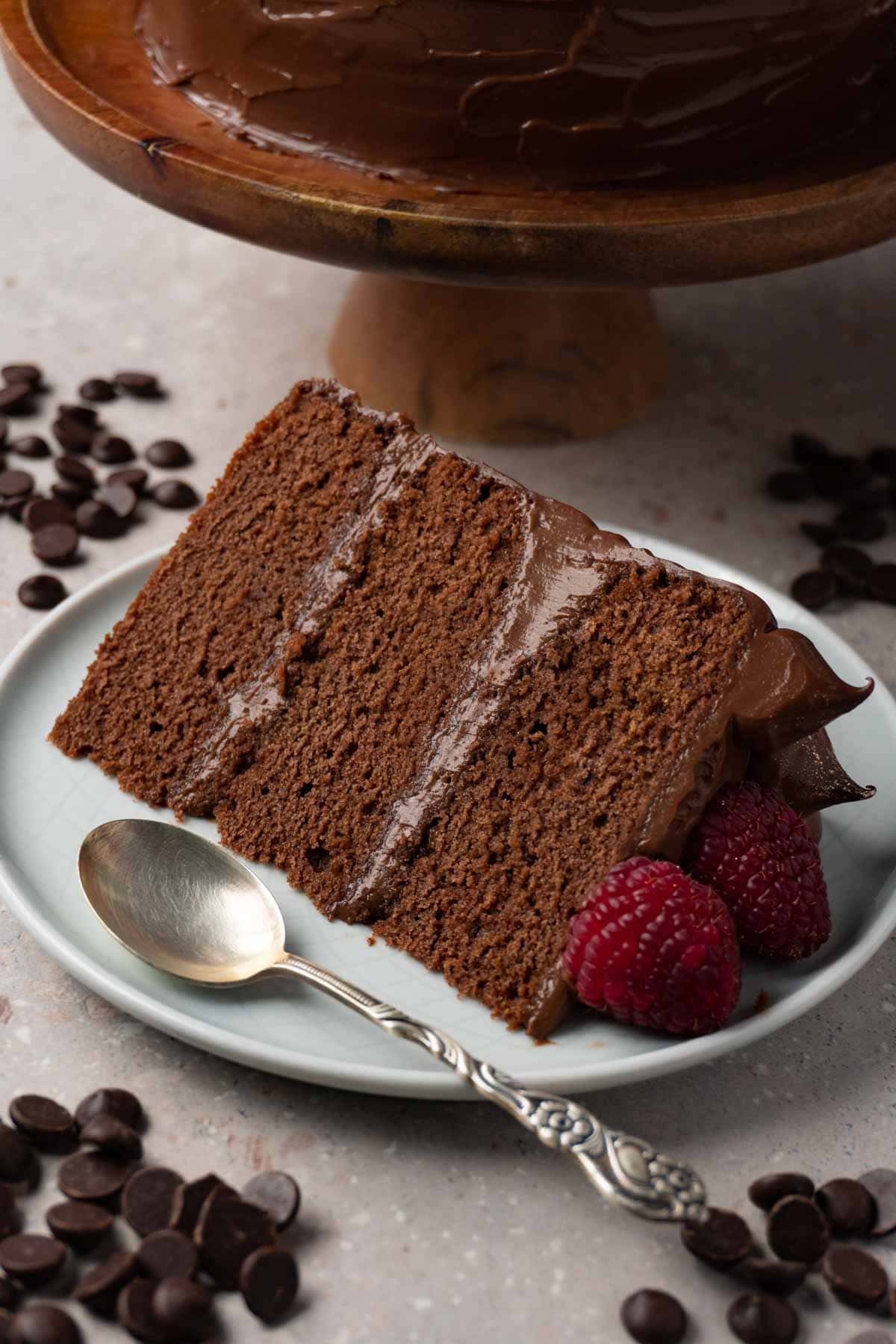 A piece of chocolate cake with fresh raspberries on a round plate, chocolate chips are lying around the plate.