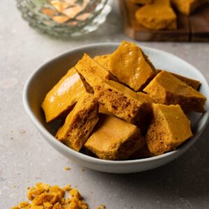 A bowl filled with honeycomb candies, crumbs of the candies are lying around the bowl.