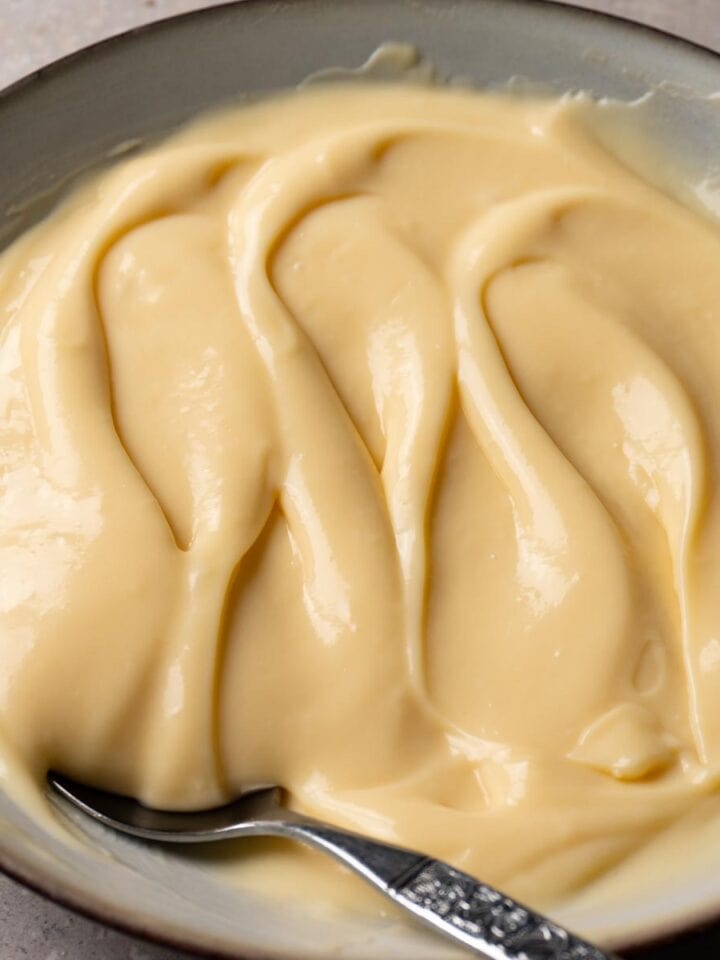 A bowl filled with pastry cream. A silver spoon is lying in the bowl.