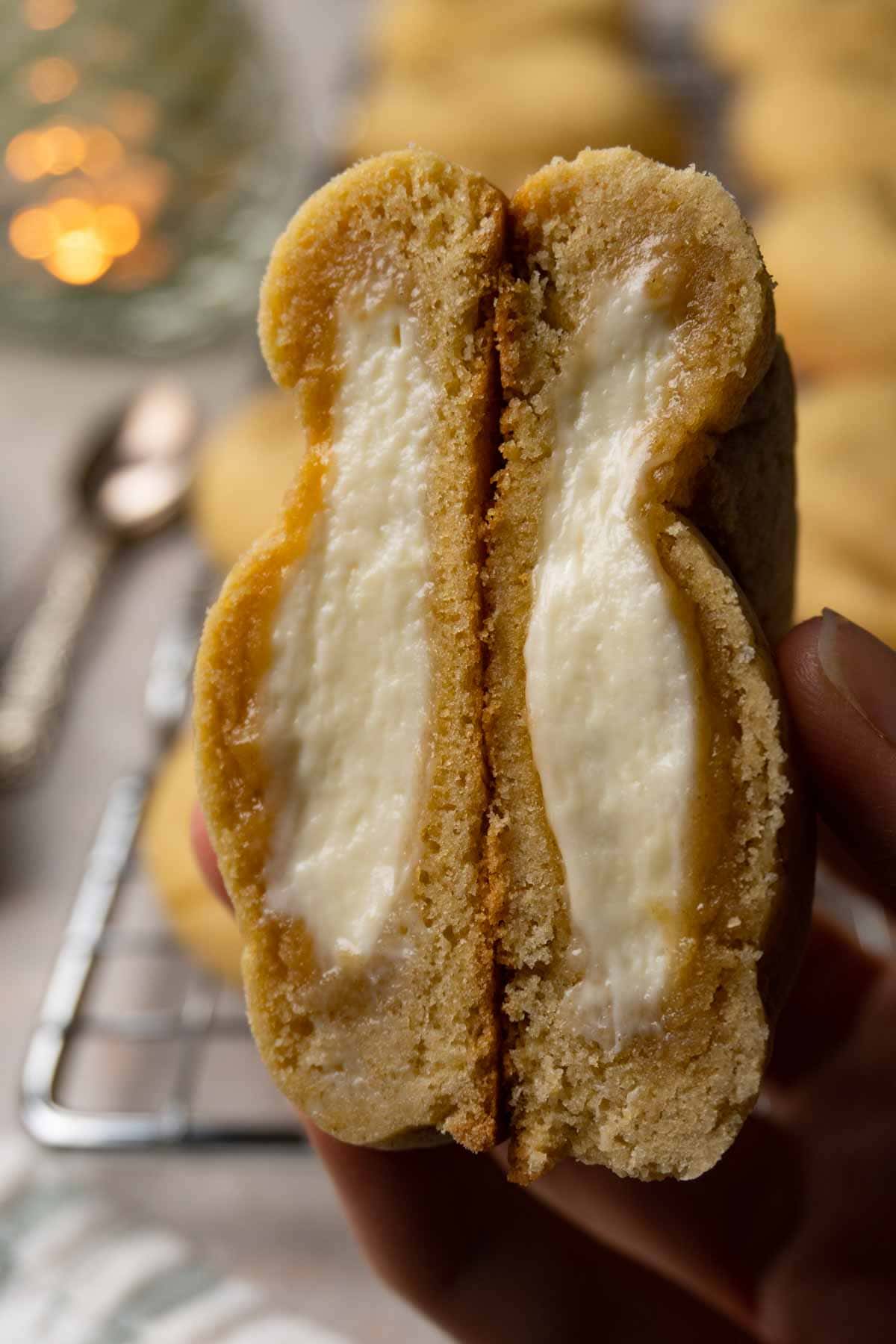 A hand is holding a cut-in-half cookie with cream cheese filling.