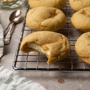 Vanilla cookies with cheesecake filling on a metal cooling rack. One bite was taken from one of the cookies.