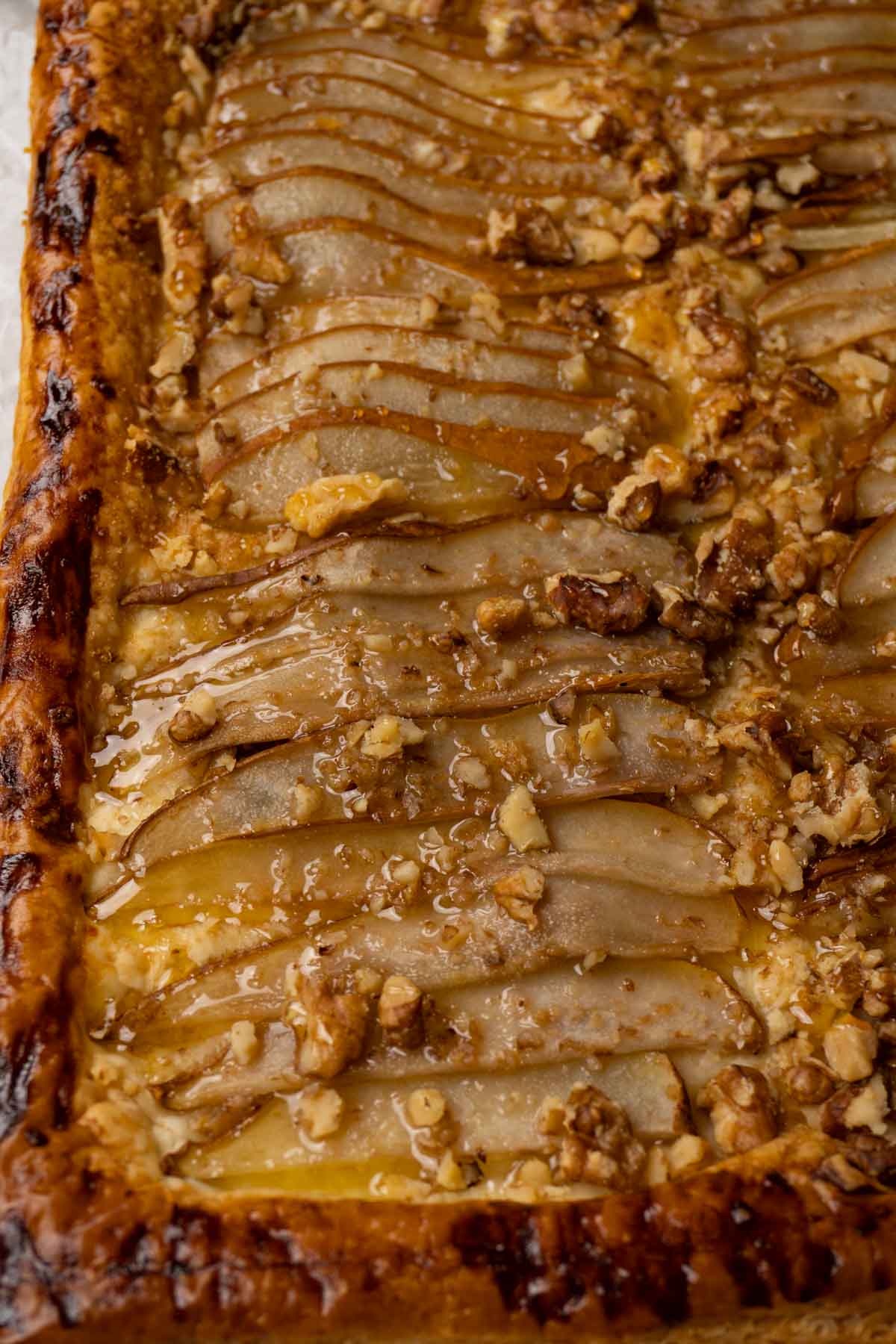 Close up shot of a tart made with puff pastry, pears, walnuts and topped with honey.