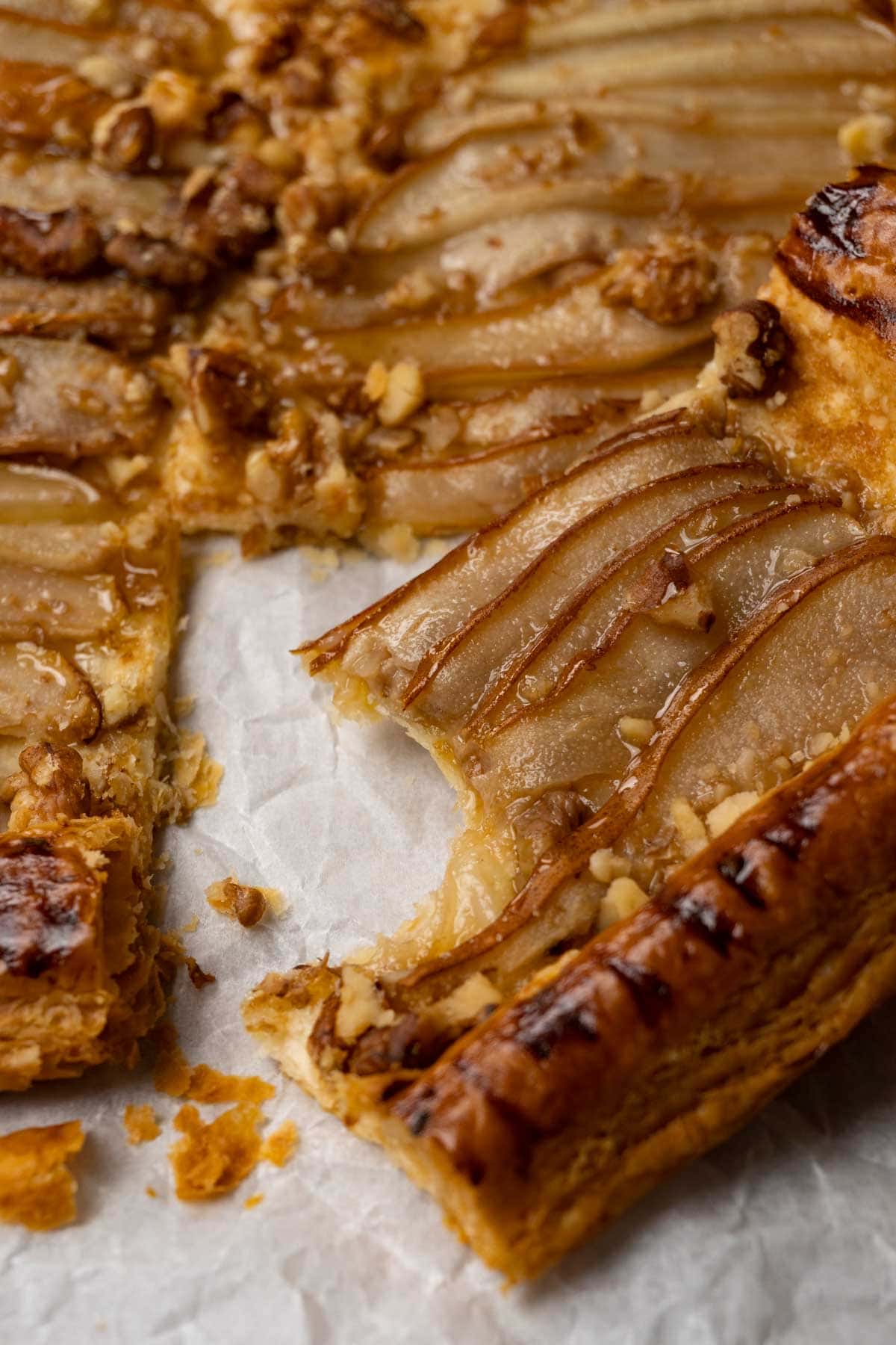 Close up shot of a tart made with puff pastry, pears, walnuts and topped with honey. One slice was cut off and one bite was taken from it.