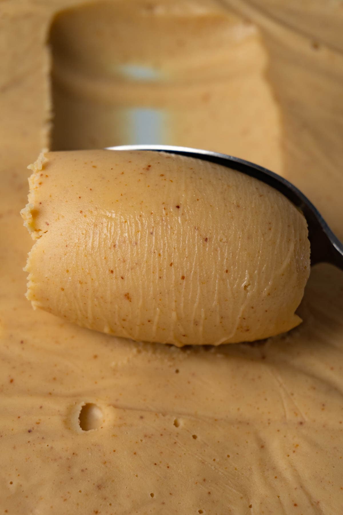 A spoon is scooping white chocolate ganache with peanut butter from a bowl.