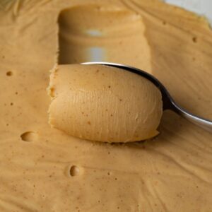 A spoon is scooping white chocolate ganache with peanut butter from a bowl.