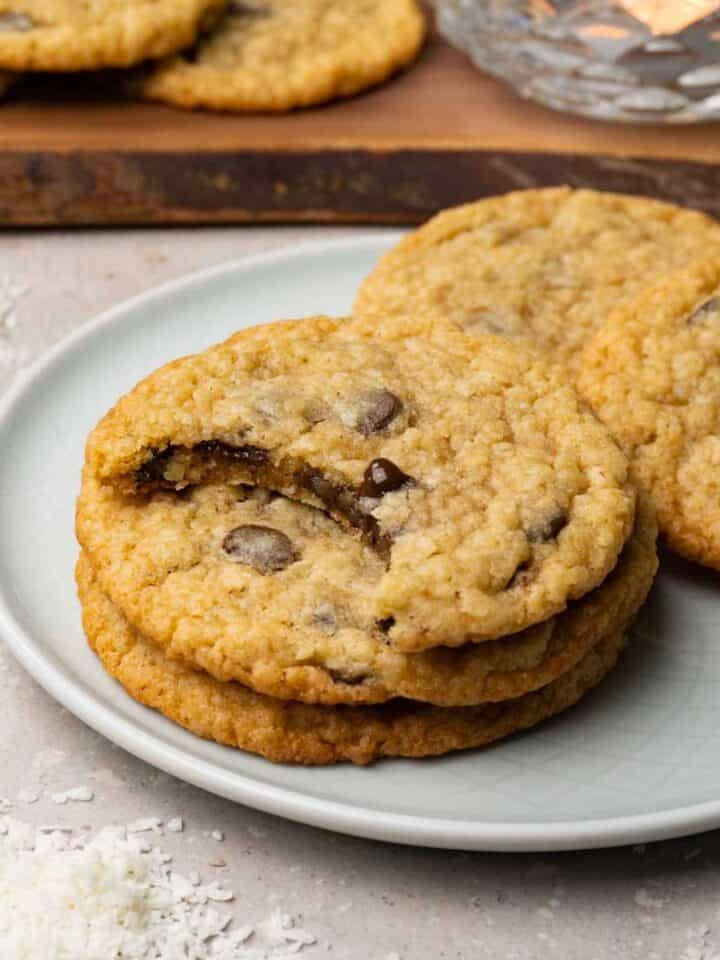Coconut cookies with chocolate chips are served on a small round plate, with one cookie showing a bite taken out of it.