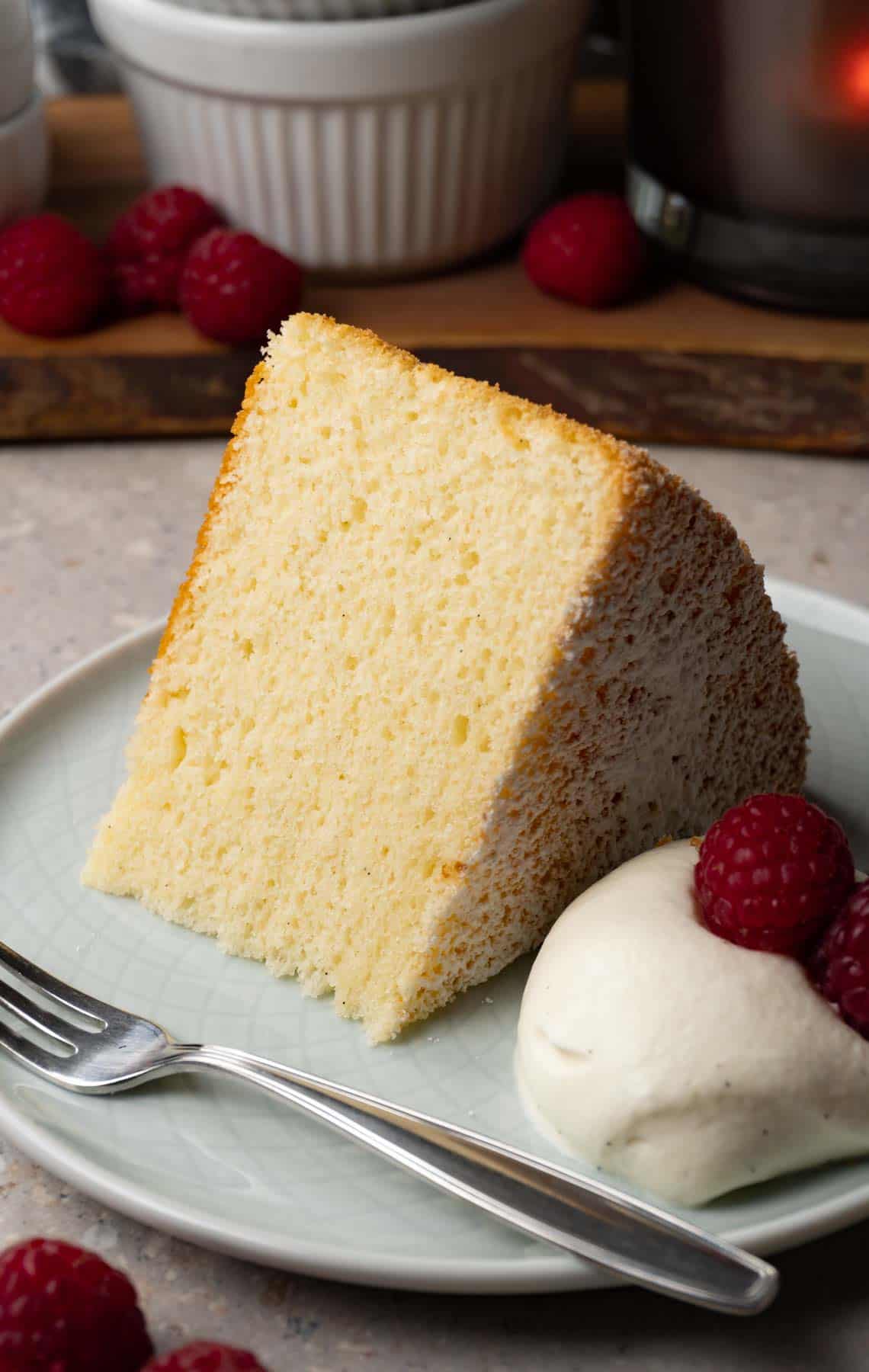 A piece of chiffon cake on a small round plate served with whipped cream and fresh raspberries.