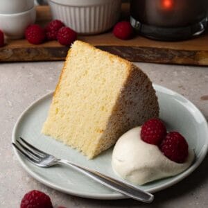 A piece of chiffon cake on a small round plate served with whipped cream and fresh raspberries.