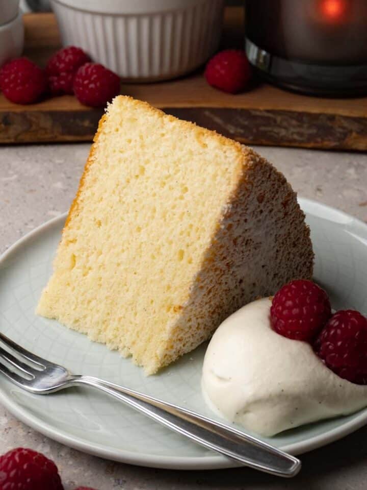 A piece of chiffon cake on a small round plate served with whipped cream and fresh raspberries.