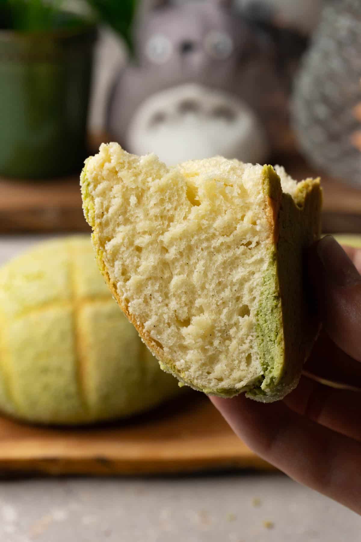 A hand is holding a piece of bread with green cookie topping.