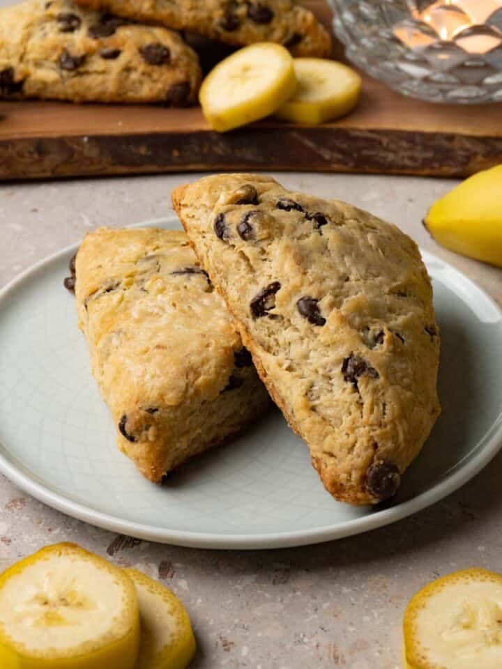 Banana scones with chocolate chips on a small round plate. Slices of fresh bananas are lying around the plate.