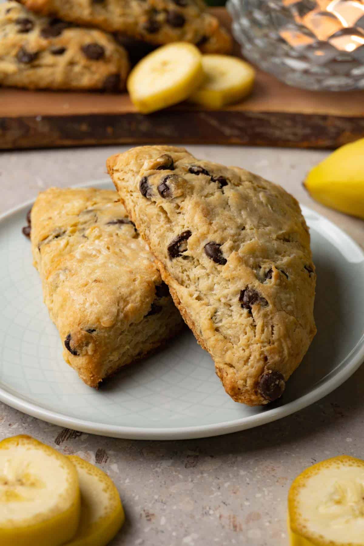 Banana scones with chocolate chips on a small round plate. Slices of fresh bananas are lying around the plate.