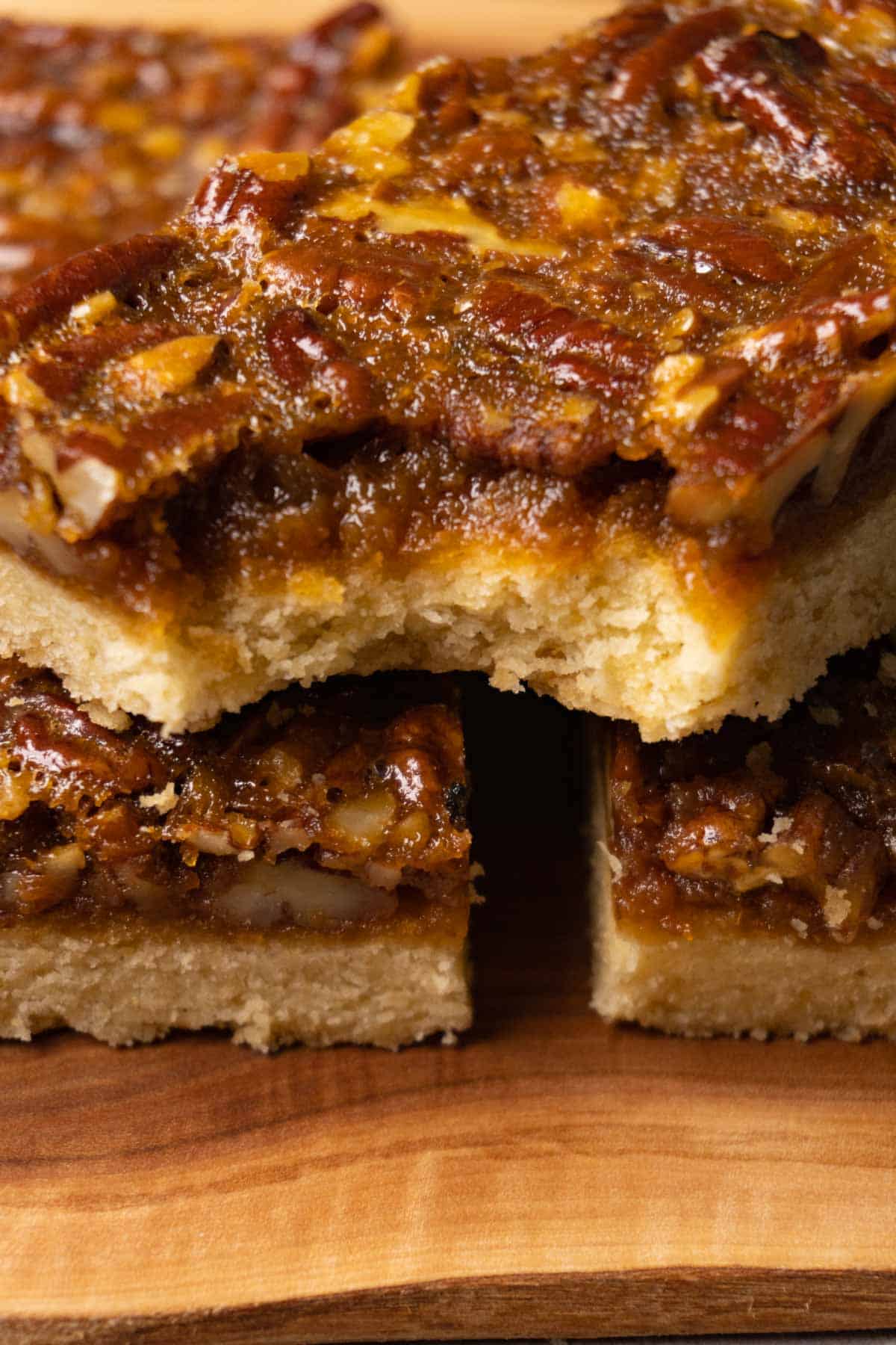 Bars with pecan filling on a wooden board, one bite taken from one of them.