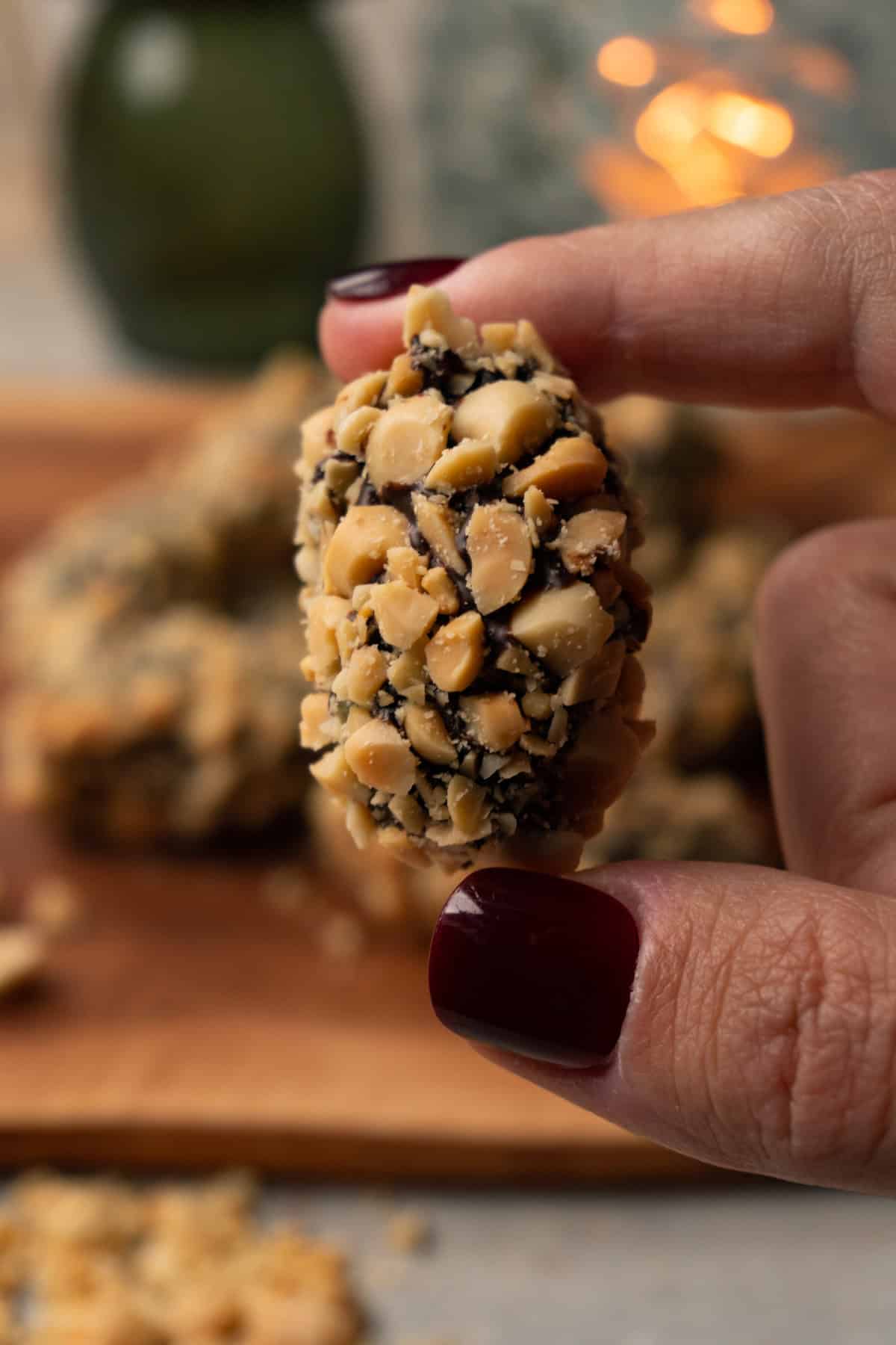 A hand holds a chocolate-covered date, coated in crushed roasted peanuts.
