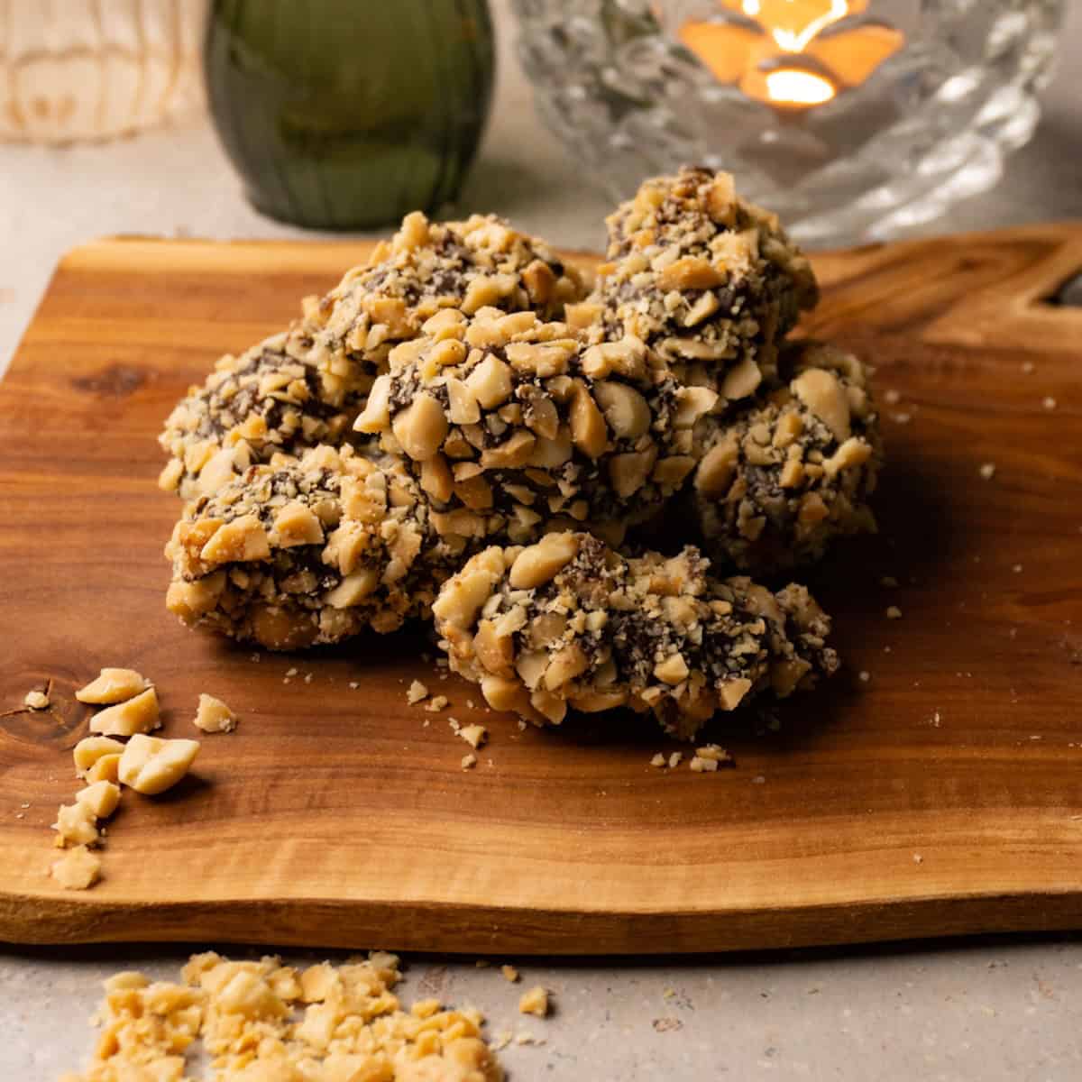 Chocolate covered dates with crushed peanuts topping on a wooden board.