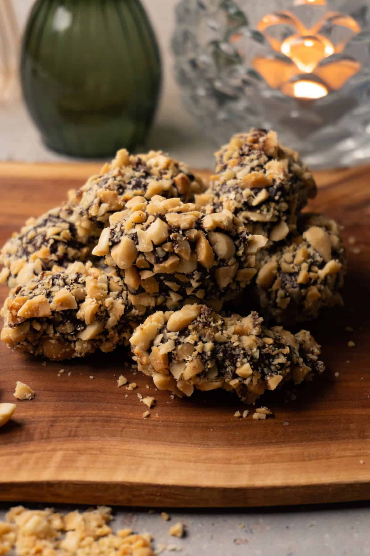 Chocolate-covered dates coated in crushed roasted peanuts are arranged on a wooden board.