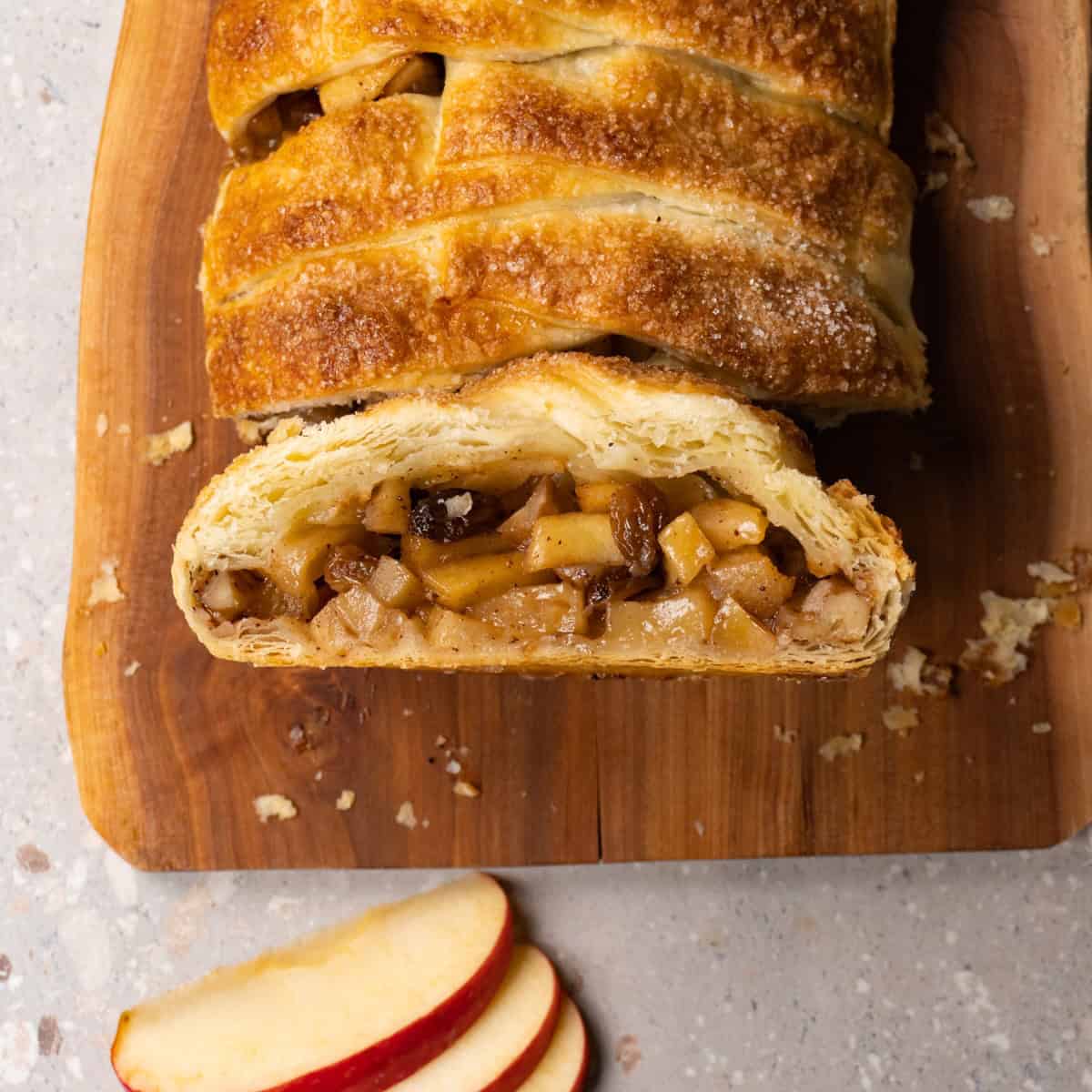 Apple pie on a wooden board, with one slice cut and placed cut side up on the board.
