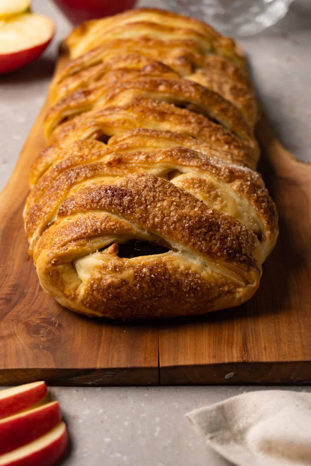 A puff pastry pie in a log shape with a braided pattern is served on a wooden board.