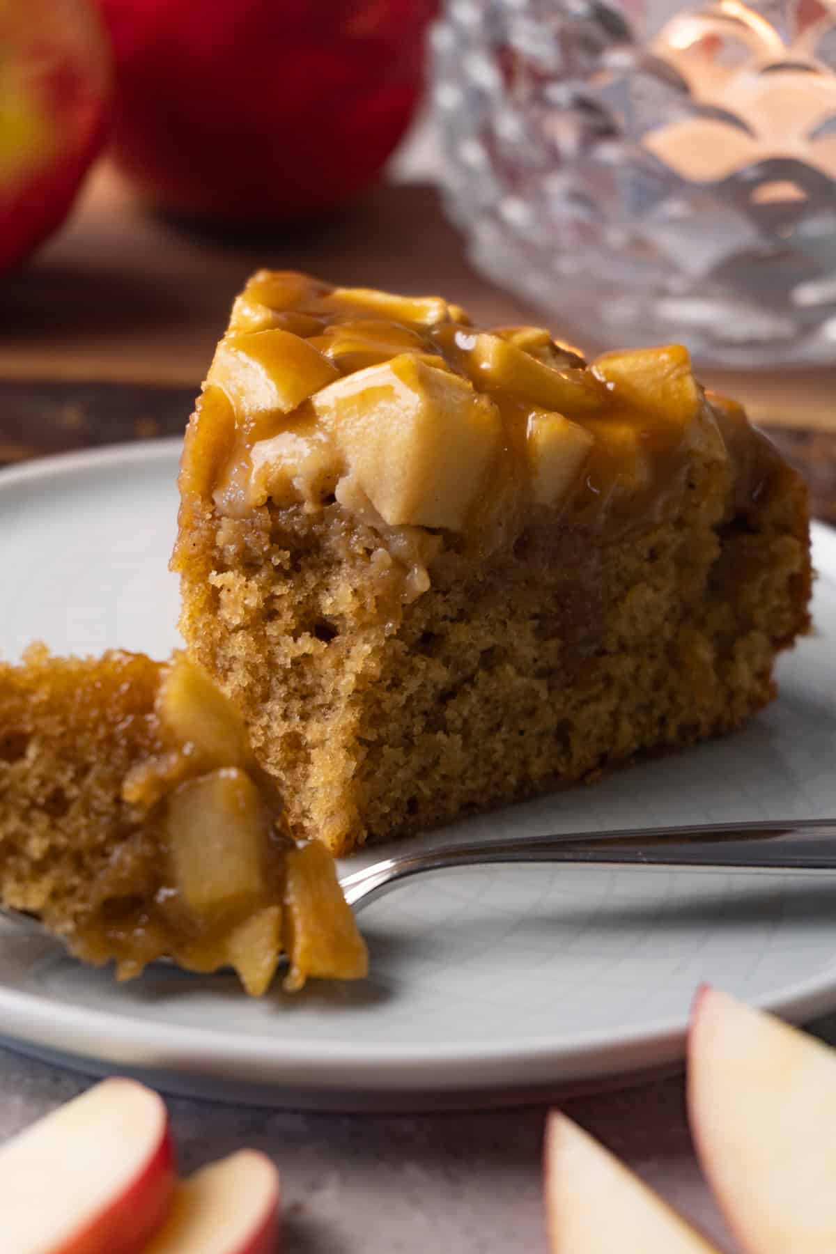 A piece of apple cake topped with toffee sauce sits on a small round plate, with one bite taken out.
