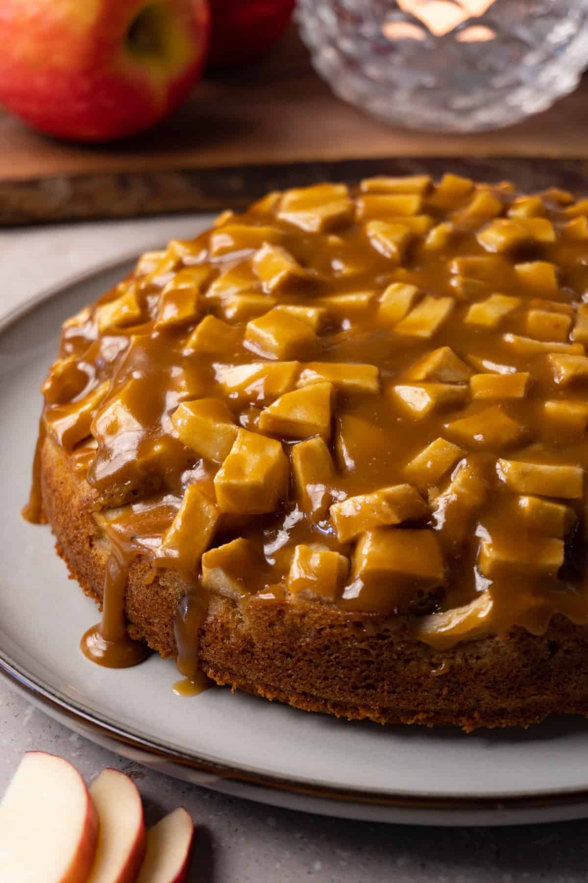 A sticky toffee apple cake sits on a large round serving plate.