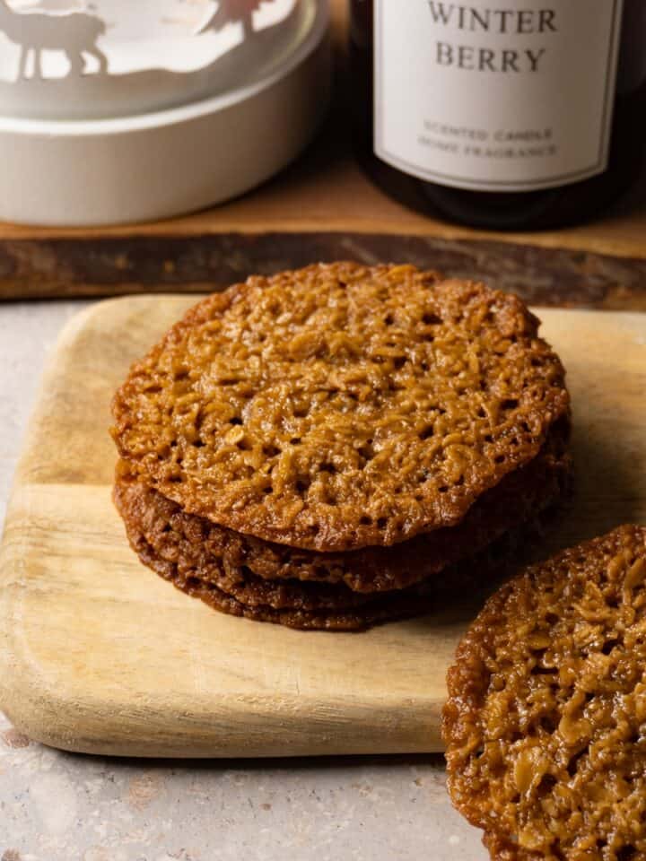 Lace cookies stacked on a wooden board.