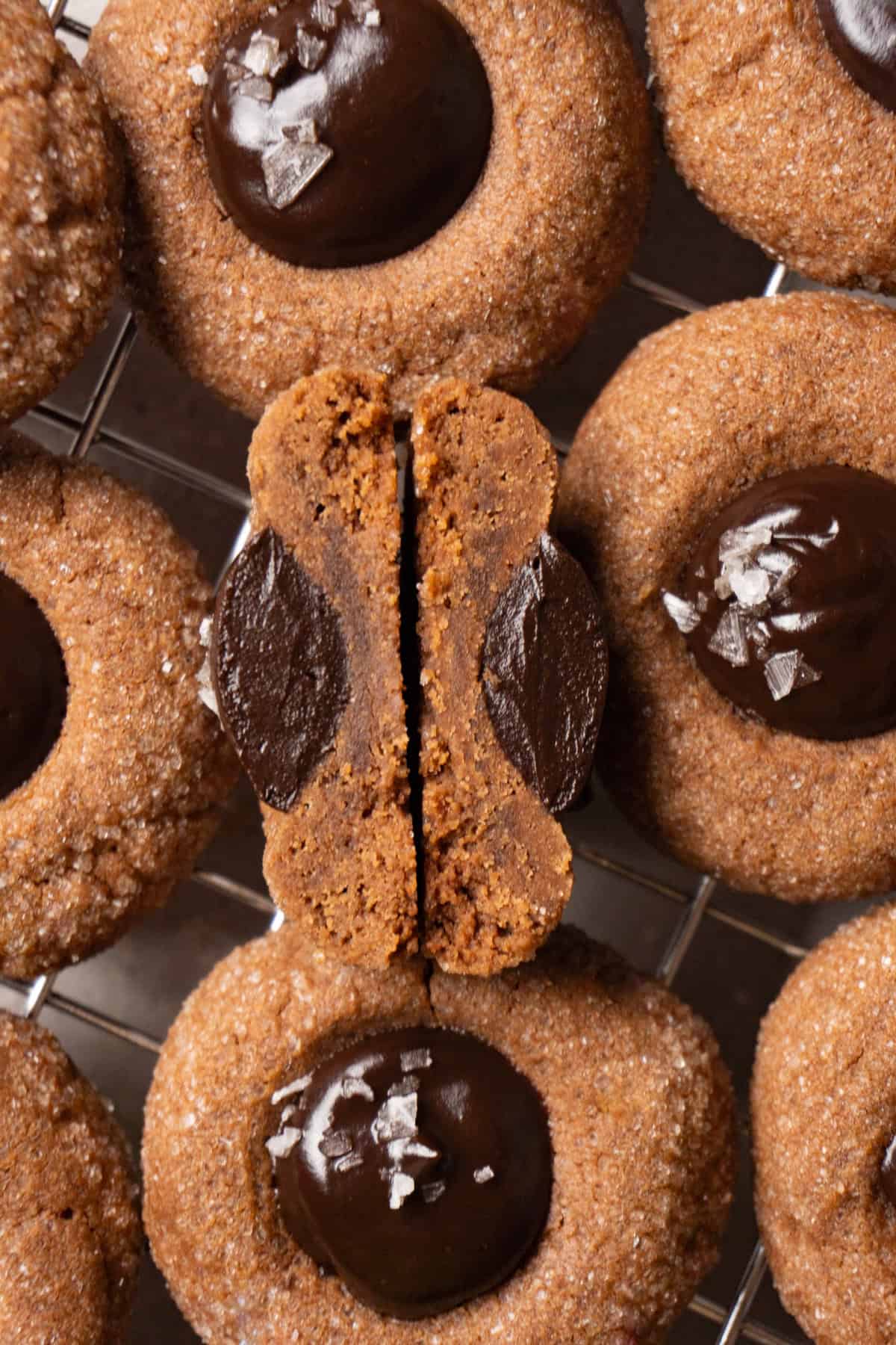 A chocolate cookie with a ganache-filled center on a metal rack. One of the cookies is cut in half.