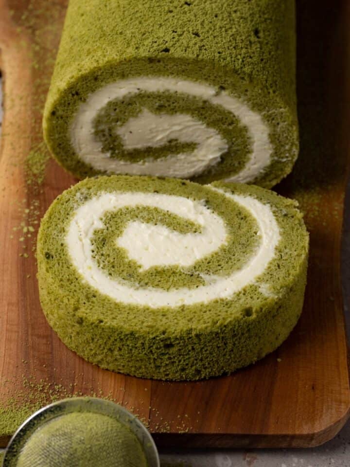 Matcha Swiss roll cake with cream cheese filling on a wooden board.
