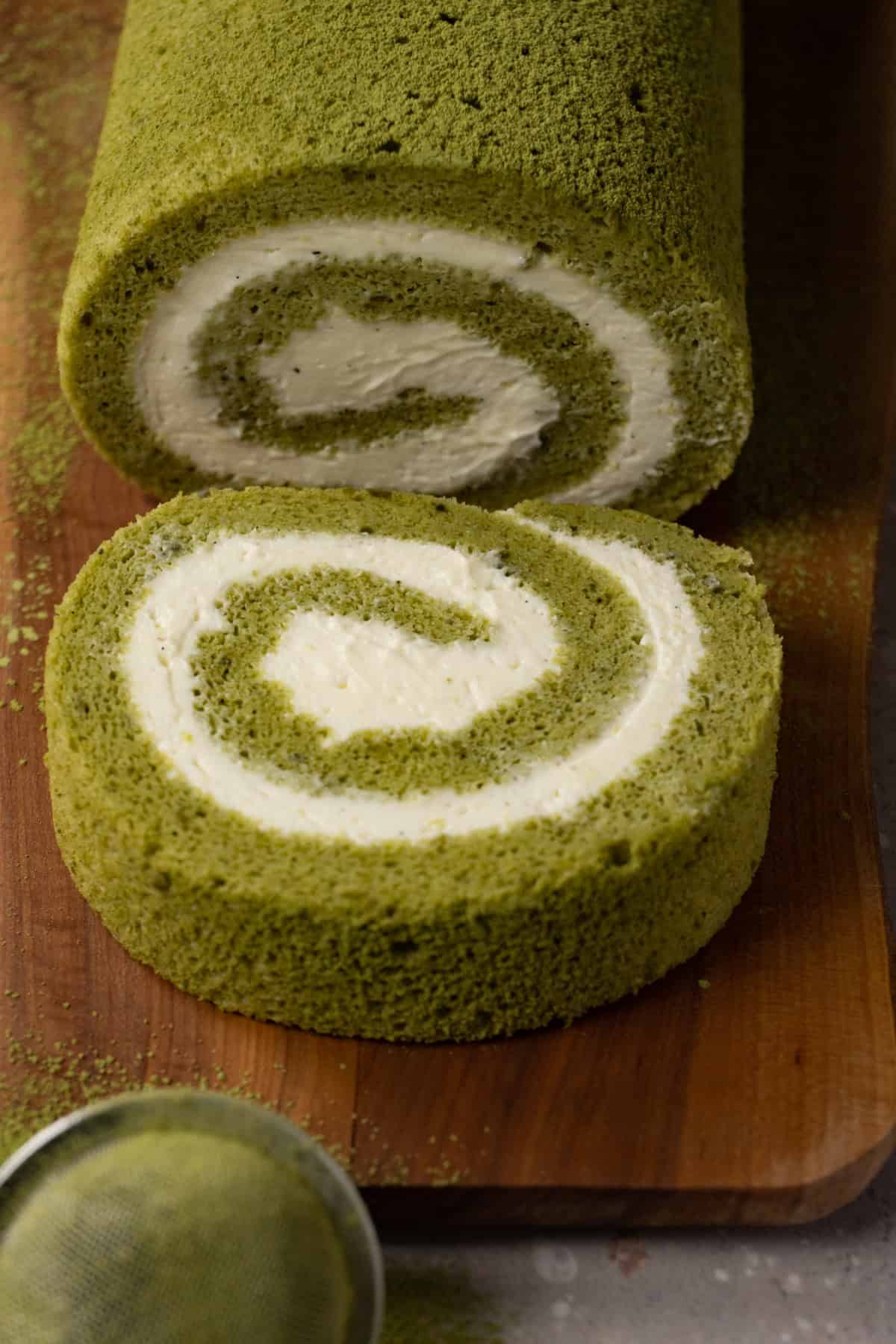 Matcha Swiss roll cake with cream cheese filling on a wooden board.