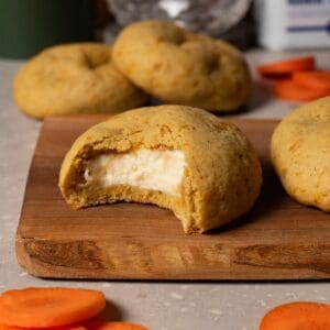 A cookie with white filling lies on a wooden board, with one bite taken out of it.