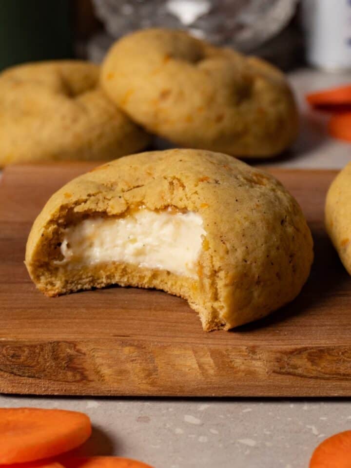 A cookie with white filling lies on a wooden board, with one bite taken out of it.