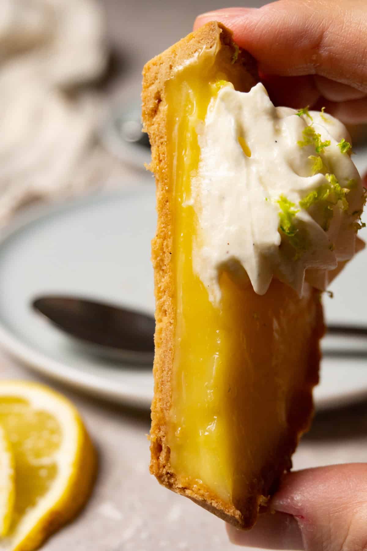 A hand is holding a halved lemon tart with a white cream topping.