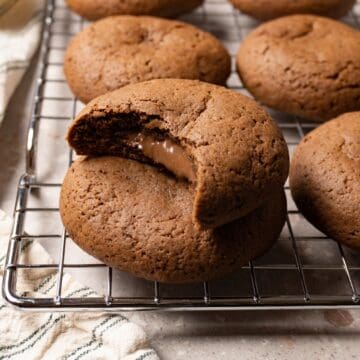 Chocolate cookies sit on a meatloaf cooling rack, with a bite taken from one cookie and chocolate filling oozing from the center.
