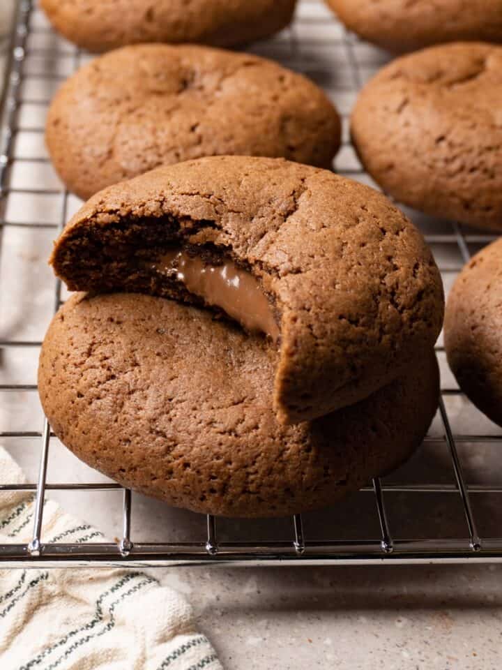 Chocolate cookies sit on a meatloaf cooling rack, with a bite taken from one cookie and chocolate filling oozing from the center.