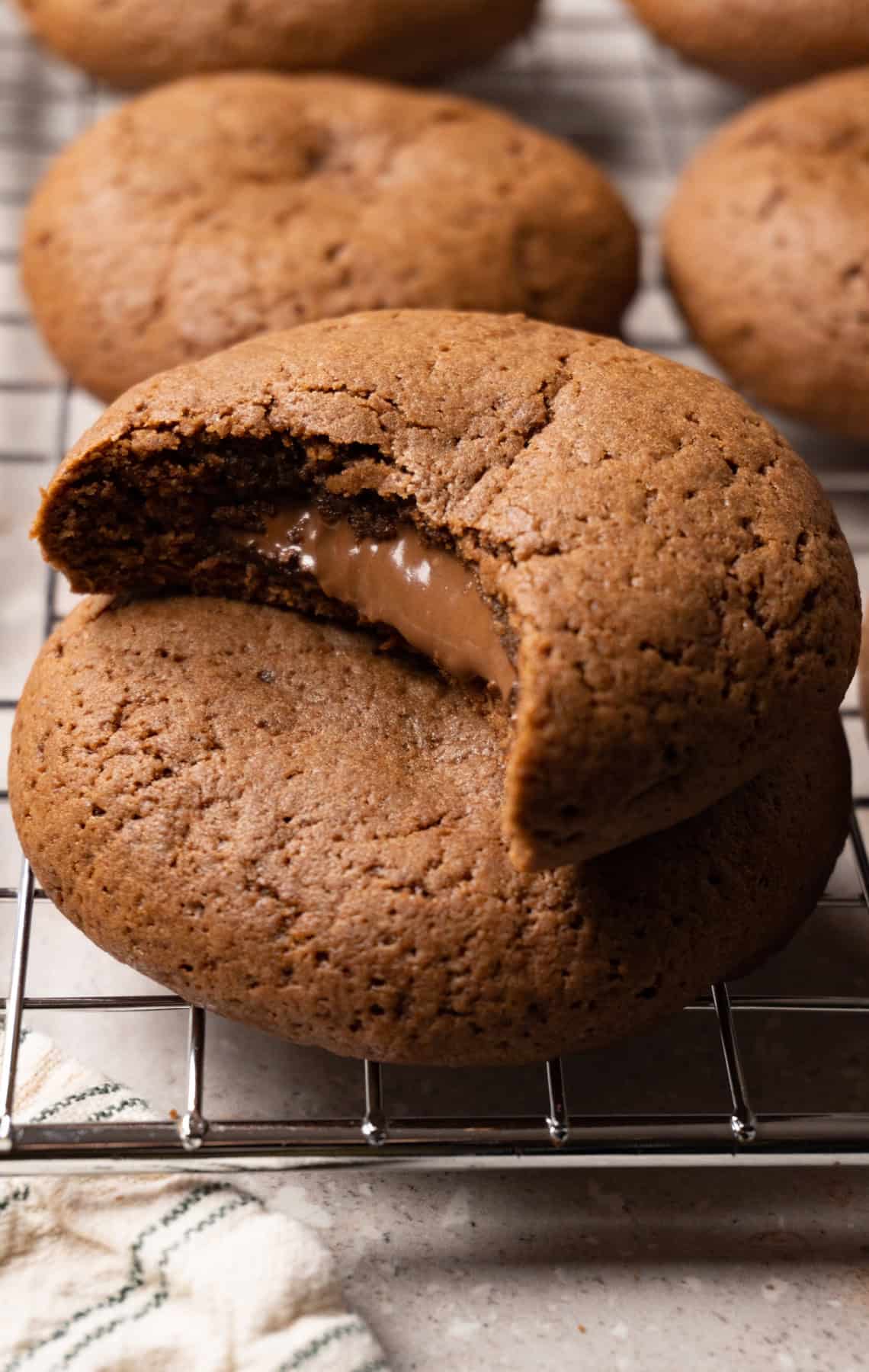 Chocolate cookies sit on a meatloaf cooling rack, with a bite taken from one cookie and chocolate filling oozing from the center.