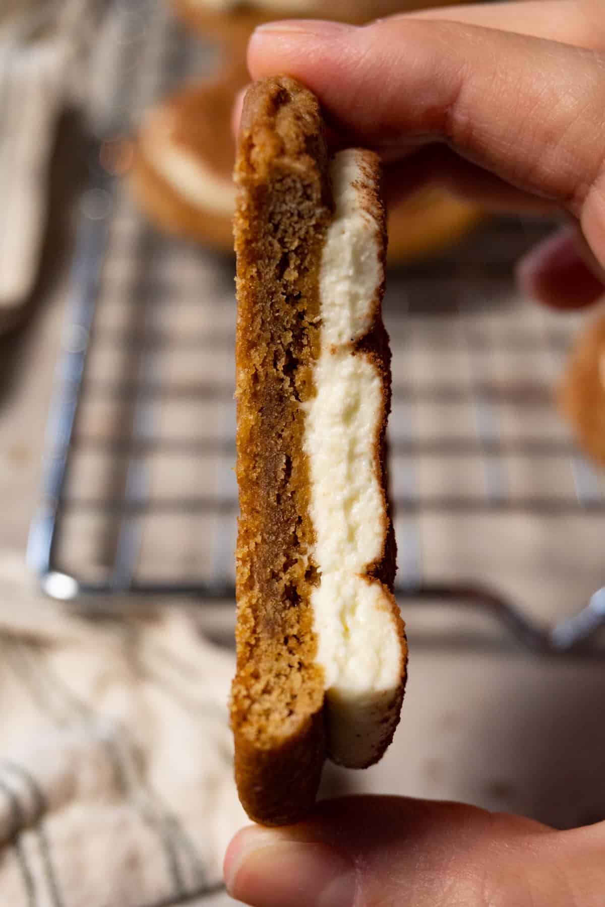 A hand holds a cookie topped with cream, with one bite taken.