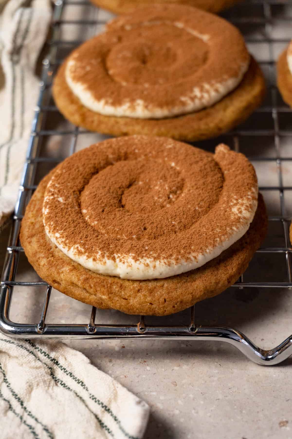 A cookie topped with cream and dusted with cocoa powder rests on a metal tray.