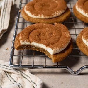 A cookie topped with cream and dusted with cocoa powder rests on a metal tray, with one bite taken.