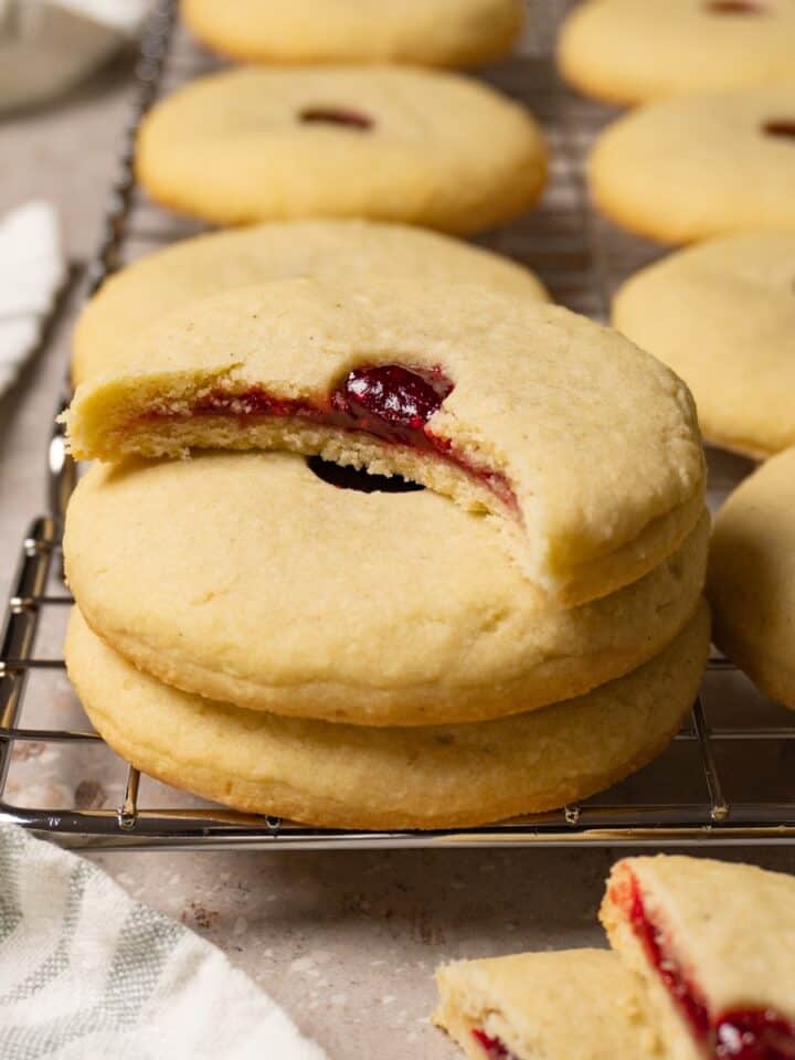 A stack of cookies filled with strawberry jam, with a bite taken from the top cookie.
