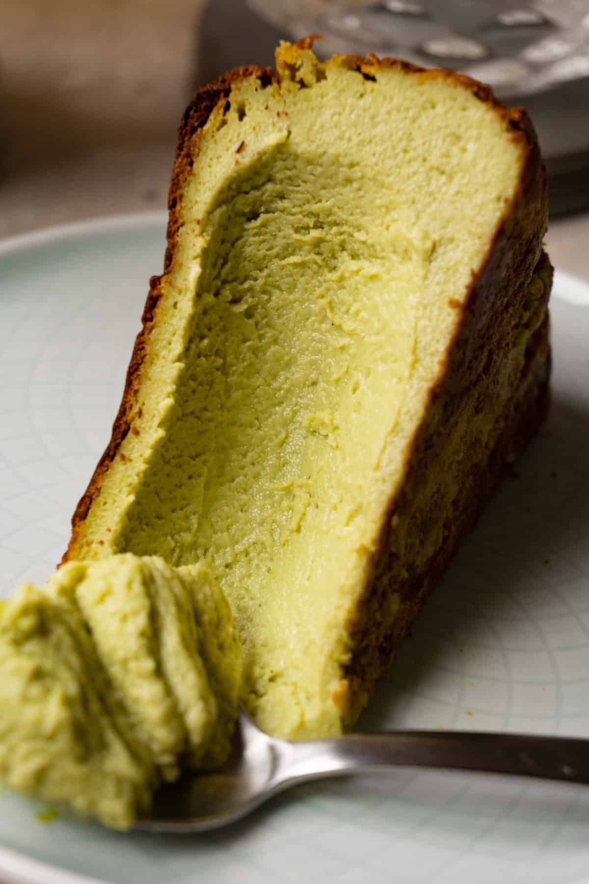 A piece of cheesecake is lying on its side on a plate, with some of it scooped out with a spoon.