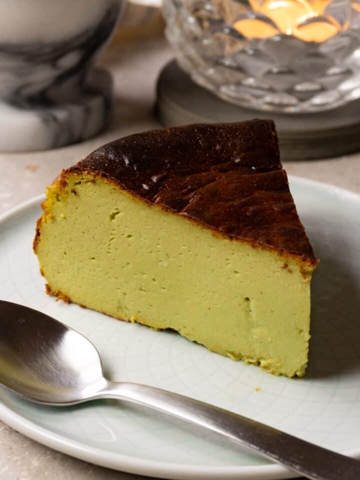 A slice of Basque matcha cheesecake is served on a plate with a silver spoon.