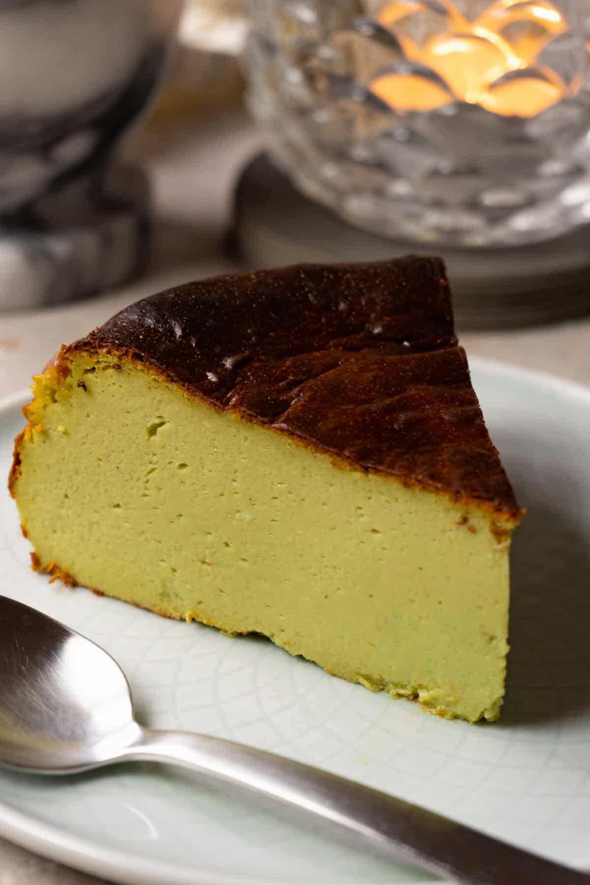 A slice of Basque matcha cheesecake is served on a plate with a silver spoon.
