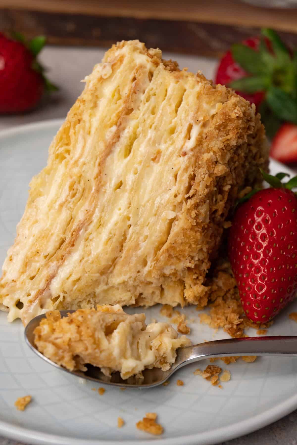 A piece of cake made with puff pastry layers and pastry cream in between, with one piece already taken using a silver spoon.