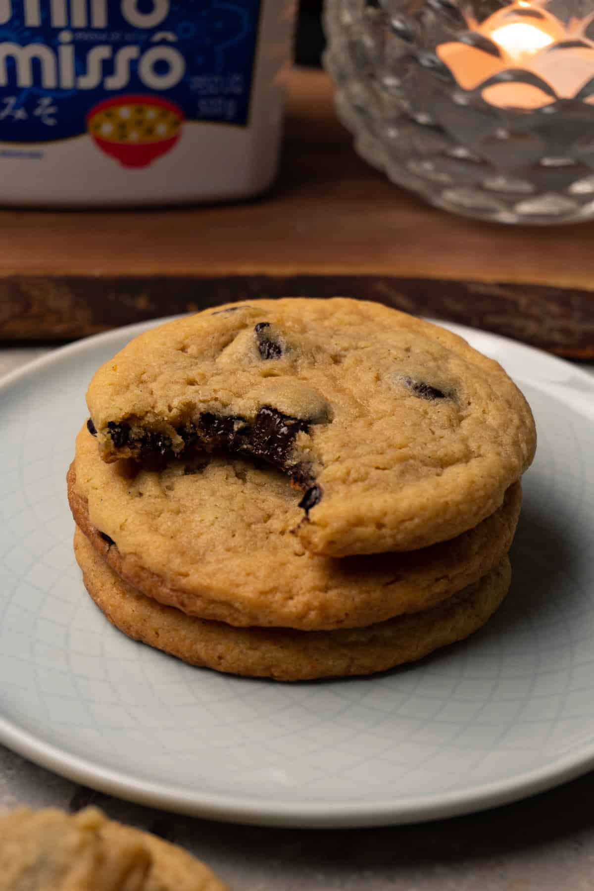A stack of chocolate chip cookies is served on a small round plate, with one bite taken from the top cookie.