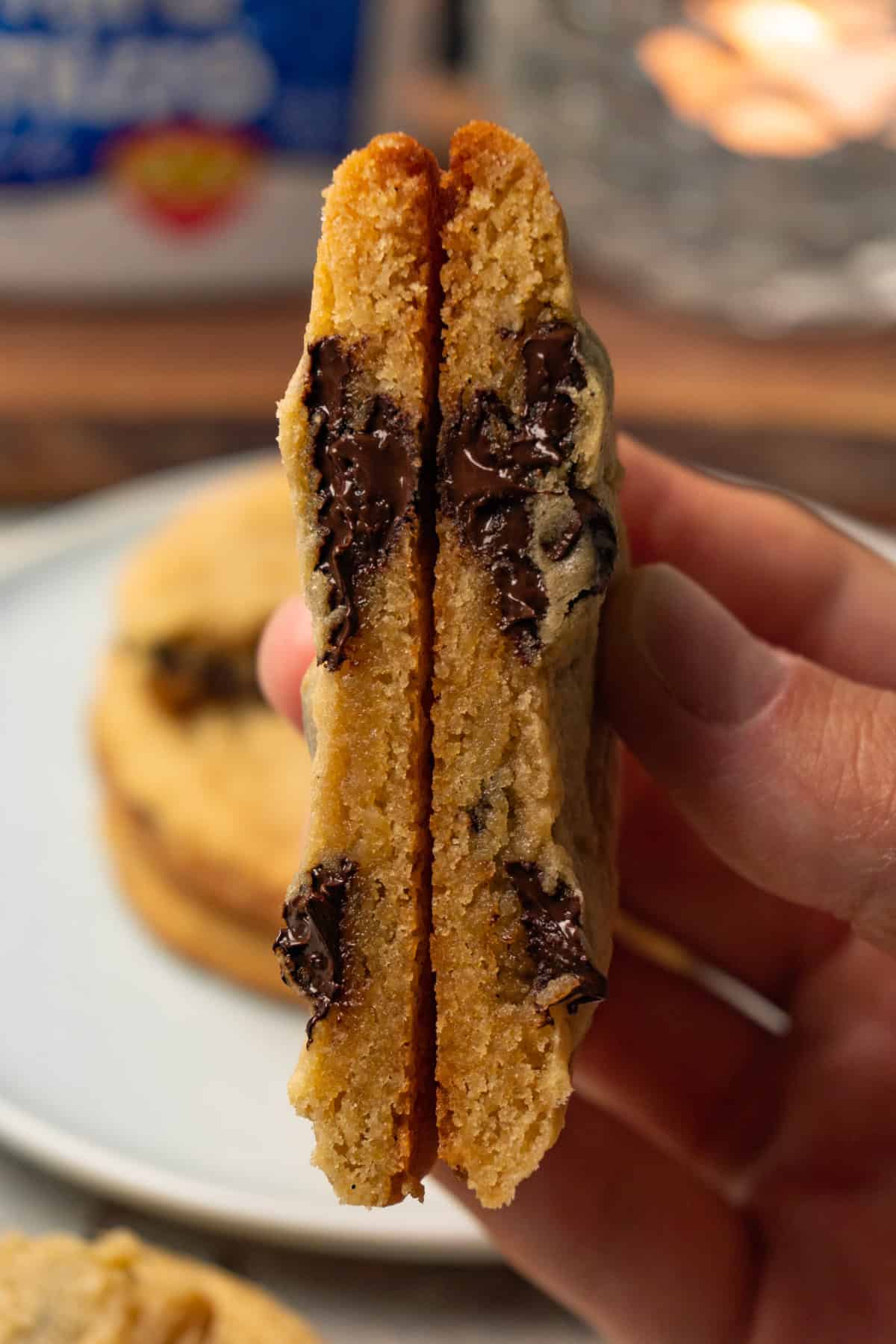 A hand is holding a chocolate chip cookie that has been cut in half.